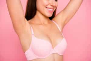 Woman in pink bra smiles celebrating her new breast profile after breast implant revision surgery.